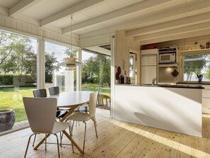Une cuisine moderne dotée d’un grand îlot central, d’un coin repas avec une table ronde et des chaises, et offrant une vue sur un jardin verdoyant grâce à de grandes fenêtres.