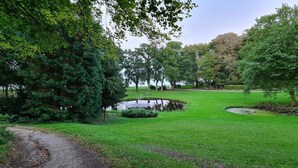 Un parc avec un étang, un sentier de gravier et différentes espèces d’arbres.