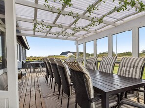 A covered outdoor seating area with a table and chairs, large windows, and a view of the landscape. - 4 Star Holiday Home in Harboore (Harboore)