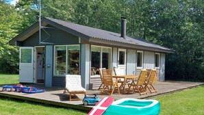 Una casa pequeña de un solo piso con porche, una mesa de comedor y sillas, y una piscina.