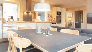 A modern kitchen with wooden cabinets, a dining table with chairs, and a hanging light fixture.