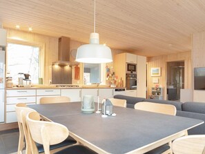 A modern kitchen with wooden cabinets, a dining table with chairs, and a hanging light fixture. - 5 Person Holiday Home in Dannemare (Dannemare)