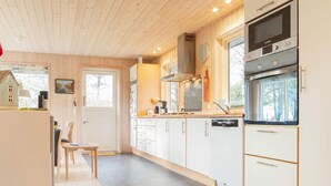 A modern kitchen with wooden cabinets, a Bosch oven, and a window overlooking a forest.