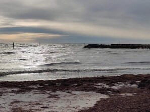A beach with rough waves and a rocky breakwater in the distance. - 5 Person Holiday Home in Dannemare (Dannemare)
