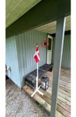 A covered porch with a metal railing, a small table, and a flagpole with a flag. - 5 Person Holiday Home in Dannemare (Dannemare)