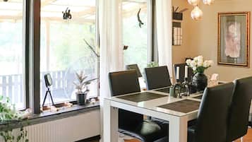 A dining area with a table set for four, chairs, a potted plant, a fan, and a framed picture on the wall.
