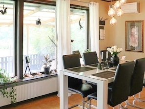 En matplats med ett bord dukat för fyra personer, stolar, en krukväxt, en fläkt och en inramad tavla på väggen.