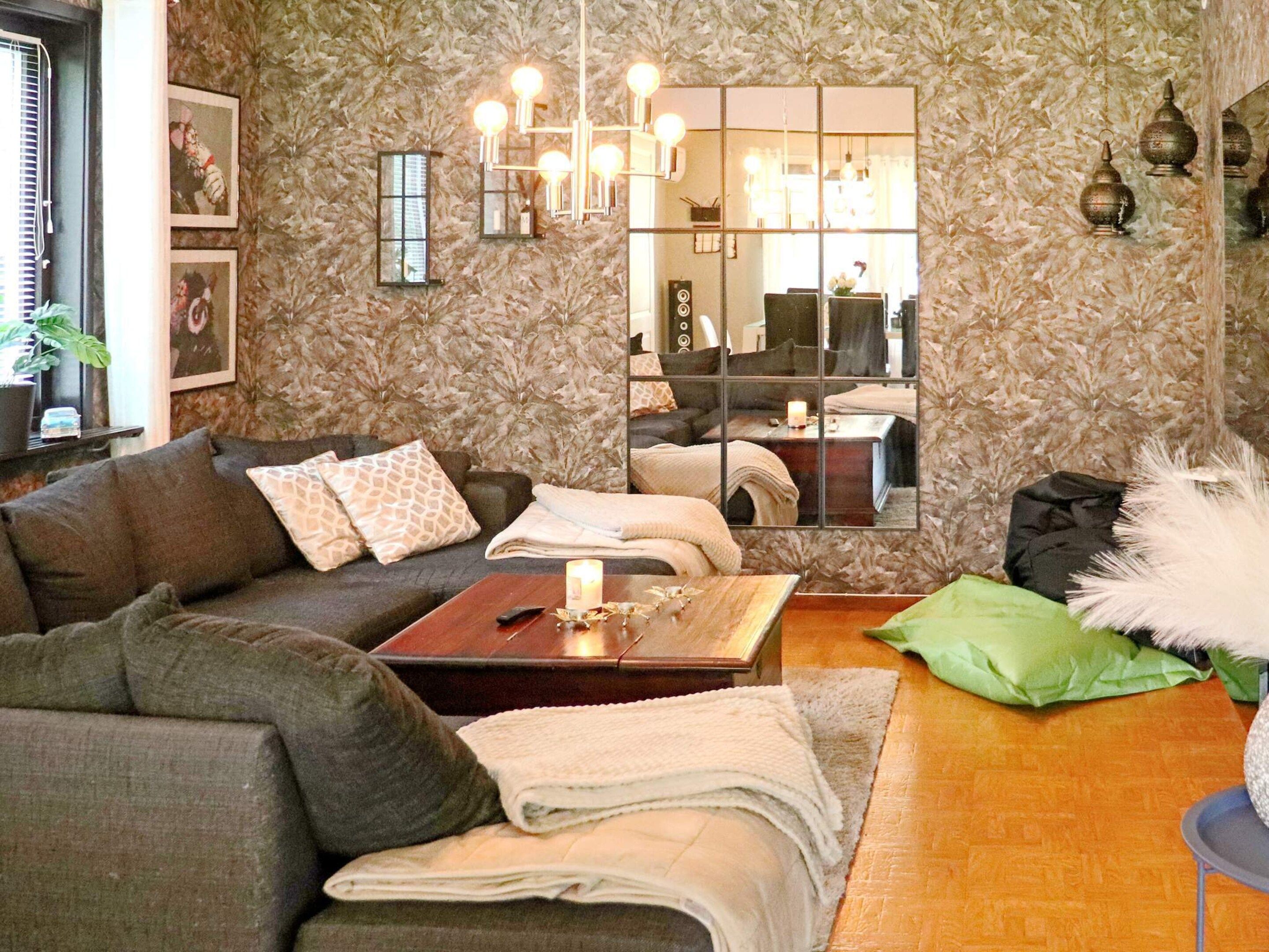 A living room with a sofa, a coffee table, a mirror, and a patterned wallpaper.