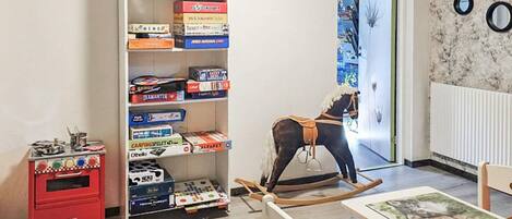 A child's playroom with a bookshelf, a rocking horse, a small table with a painting, and a red storage unit.