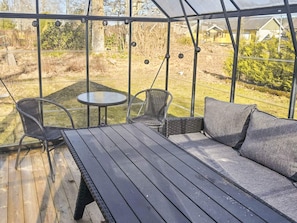 Ett takförsett utomhusområde med bord och stolar, med utsikt över en trädgård och ett bostadsområde.