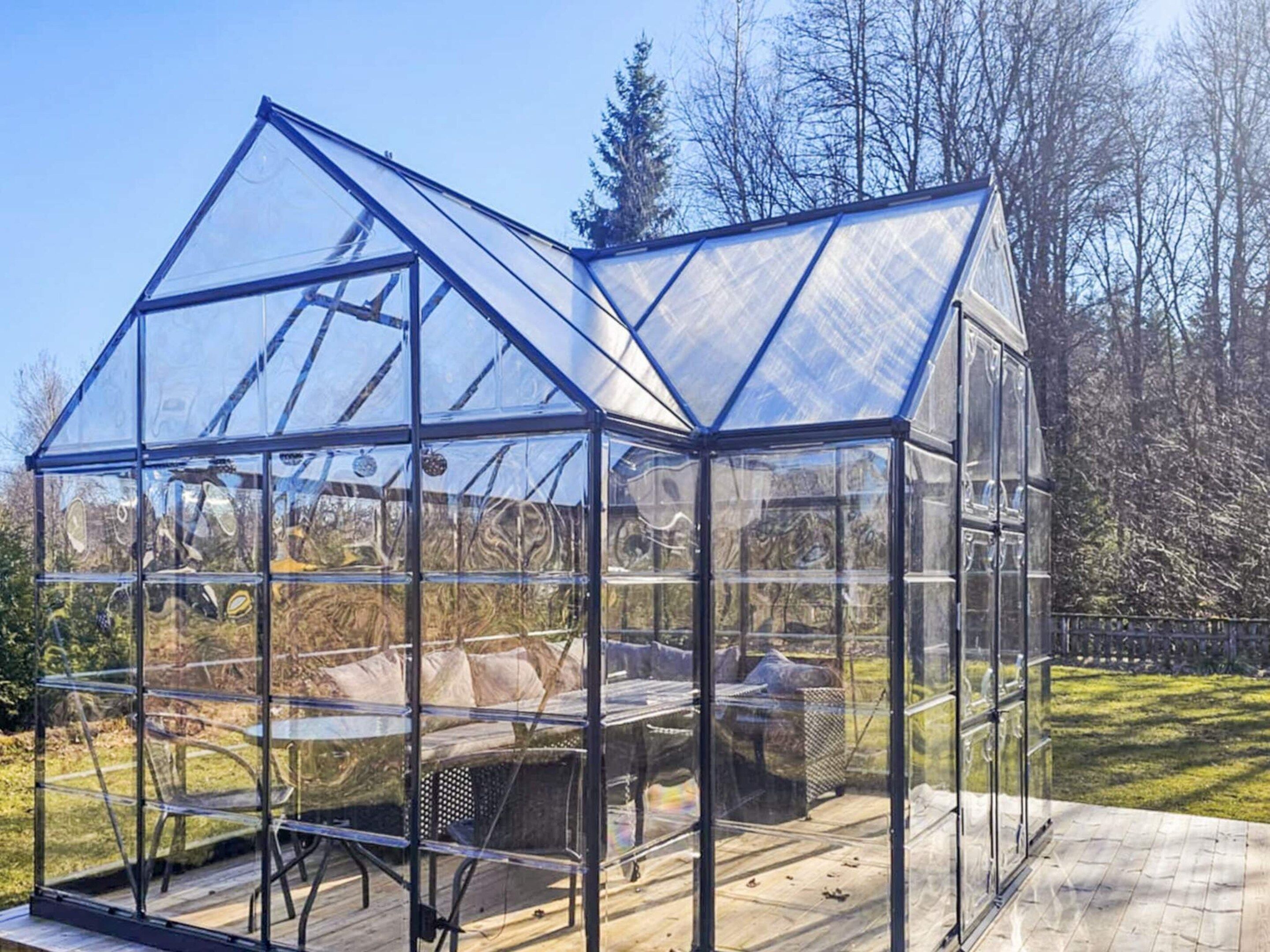 Estructura de invernadero transparente con techo y paredes, una banca en el interior y una terraza de madera en el exterior.