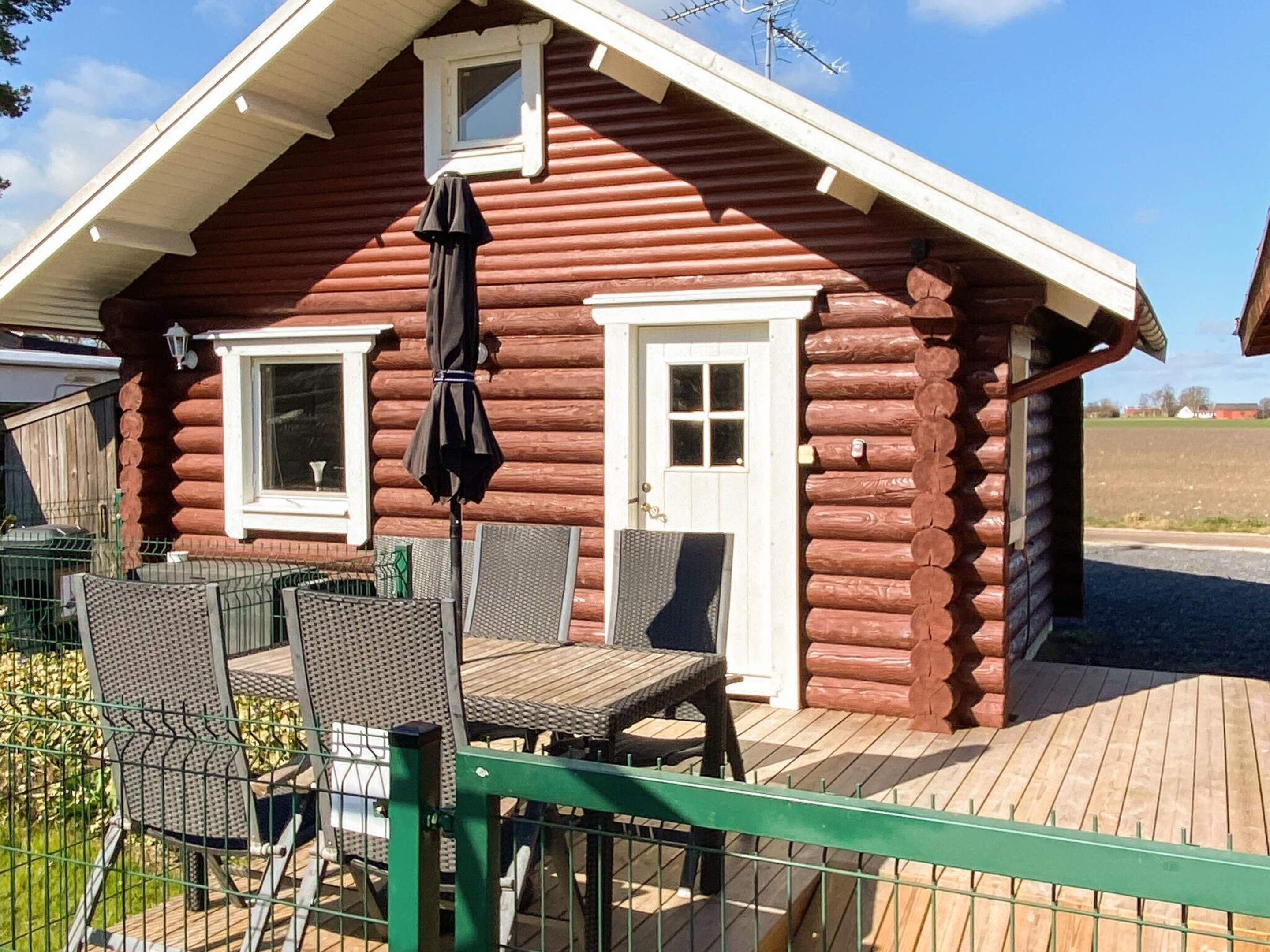 A log cabin with a deck, two windows, and a small porch area with a table and chairs.