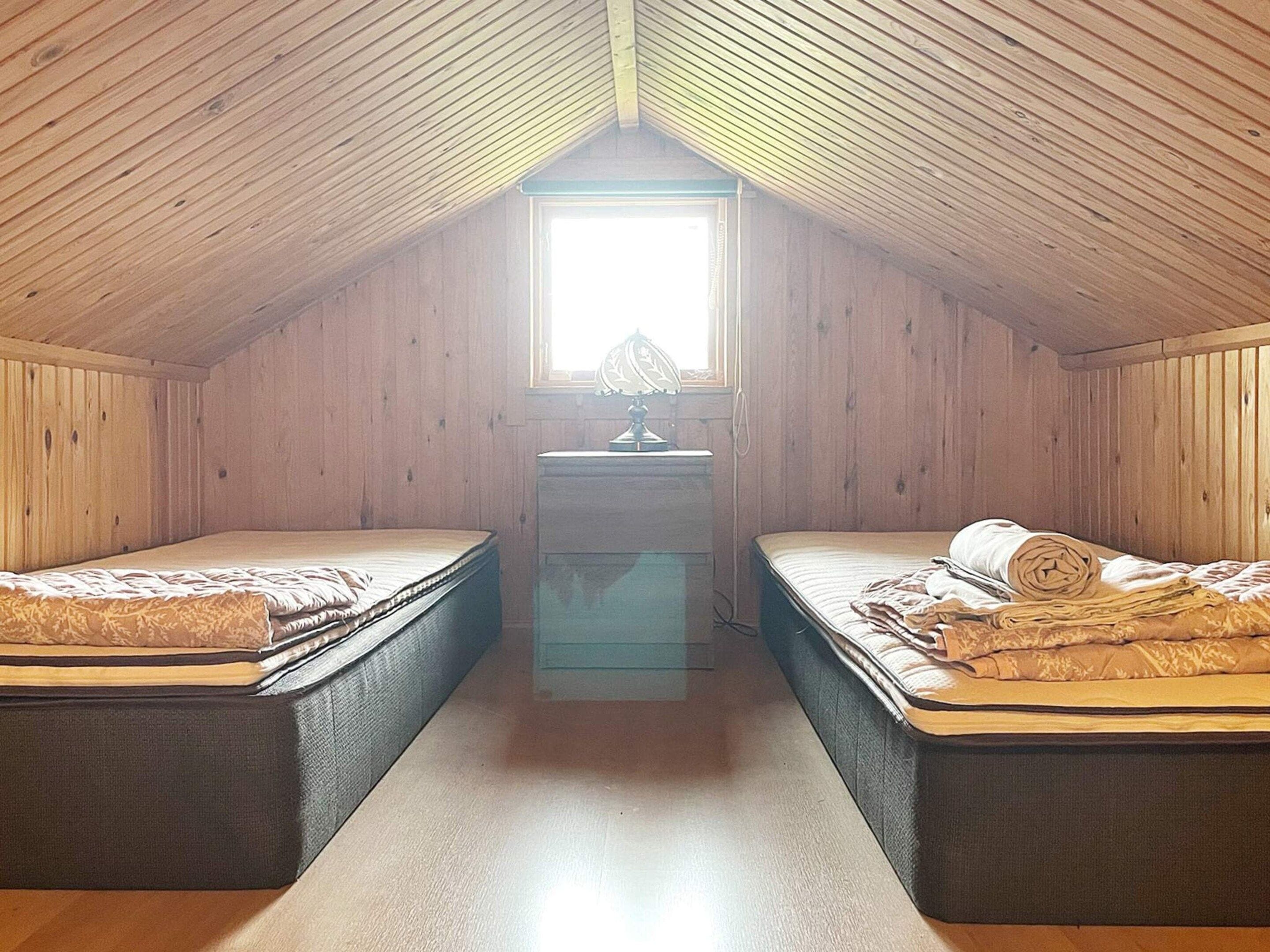 A small attic bedroom with two beds, a desk, and a window.
