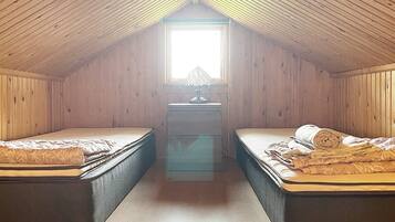 A small attic bedroom with two beds, a desk, and a window.