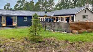 Eine Hütte mit überdachter Sitzgruppe, einem eingezäunten Garten und einem kleinen Baum.