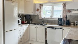 A compact kitchen with white cabinetry, a built-in dishwasher, and a window with curtains. - 4 Star Holiday Home in Ingaro (Ingaro)