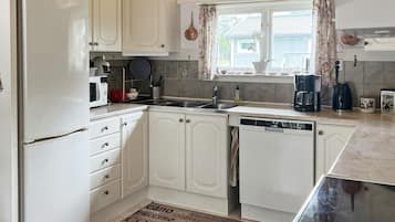 A compact kitchen with white cabinetry, a built-in dishwasher, and a window with curtains.