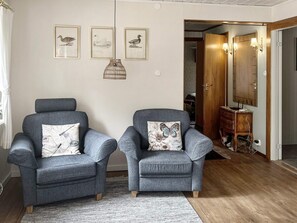 A living room with two grey armchairs, a patterned rug, and wall-mounted artwork.