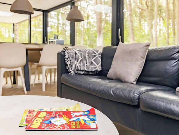 A modern living room with a leather sofa, a round coffee table, and a dining area with chairs and a table.
