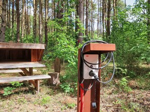 A portable generator with a control panel and a red cable, located outdoors near a wooden picnic table and a tree stump.