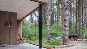 Una cabaña moderna con terraza de hormigón, paredes de madera y vistas a un bosque.