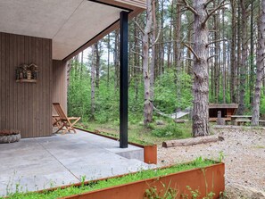 Una cabaña moderna con terraza de hormigón, paredes de madera y vistas a un bosque.
