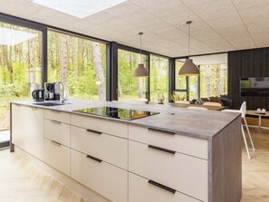 A modern kitchen with a large island, built-in appliances, and large windows offering a forest view.
