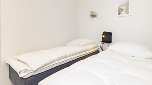 Una habitación pequeña y limpia con dos camas individuales, una mesita de noche con lámpara y dos cuadros en la pared.