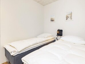 Una habitación pequeña y limpia con dos camas individuales, una mesita de noche con lámpara y dos cuadros en la pared.