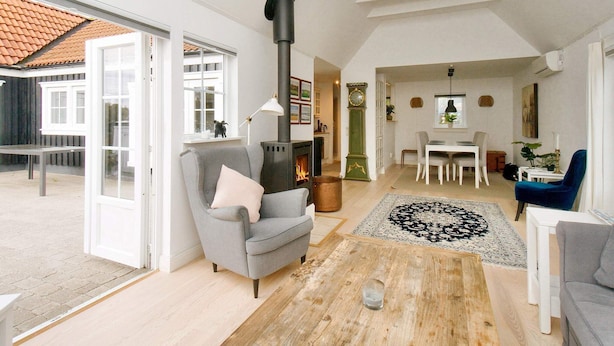 A spacious living room with a fireplace, a dining area, and a large window. - 4 Star Holiday Home in Vejby (Vejby)
