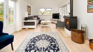 A spacious living room with a sofa, a coffee table, a TV, a fireplace, and a large window. - 4 Star Holiday Home in Vejby (Vejby)