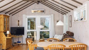 A cozy room with a wooden dining table, chairs, a television, and a large window with curtains.