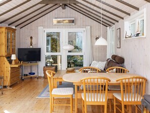 Ett mysigt rum med ett matbord och stolar i trä, en tv och ett stort fönster med gardiner.