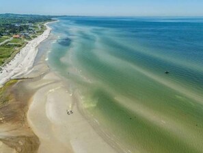 En vy över en strand sedd från luften, med klart vatten och en sandstrand.