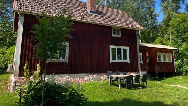 Une maison en bois rouge avec un toit en tuiles, une petite dépendance attenante et un patio avec des meubles d ’extérieur.