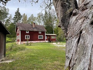 A red wooden house with a sloped roof and a chimney, surrounded by a grassy yard and trees. - 6 Person Holiday Home in Asarum (Asarum)