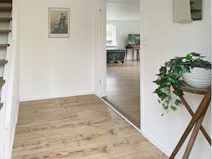 A hallway with wooden flooring, a framed picture on the wall, and a potted plant on a stand. - 6 Person Holiday Home in Asarum (Asarum)