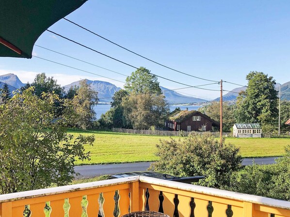 A rural landscape with a house, a small greenhouse, and mountains in the background.