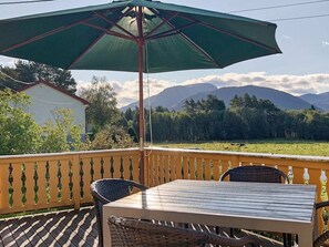 A balcony with a table and chairs, an umbrella, and a view of mountains.