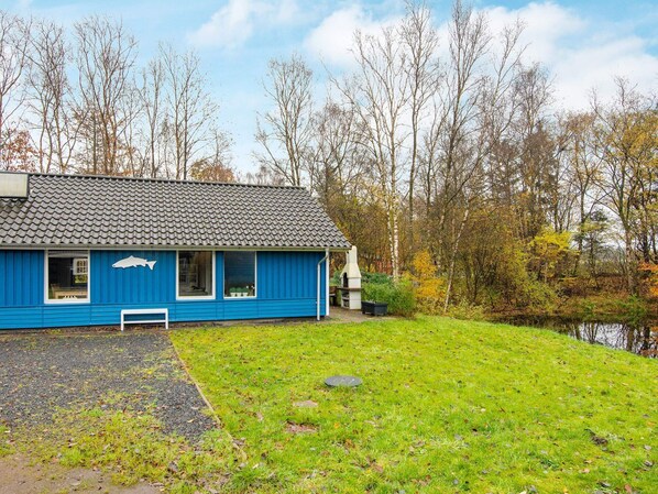 Un bâtiment bleu avec un toit recouvert de tuiles, un banc et un petit étang en arrière-plan.