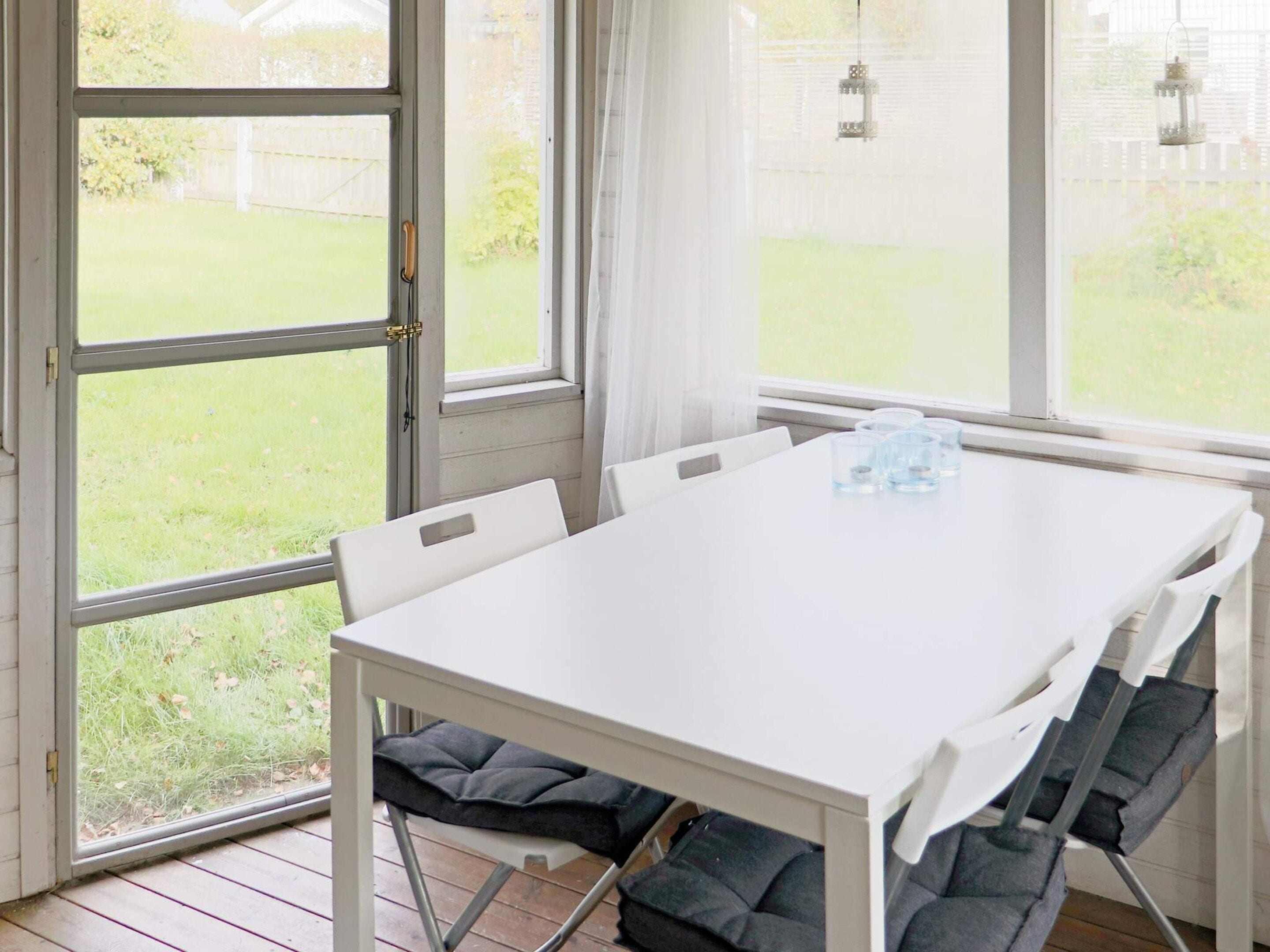 A white table with four chairs, a window with a view of a grassy yard, and a door with a handle.