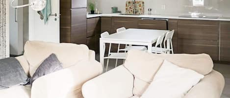 Une cuisine moderne avec une table et des chaises blanches, un réfrigérateur et une fenêtre au-dessus de l’évier.