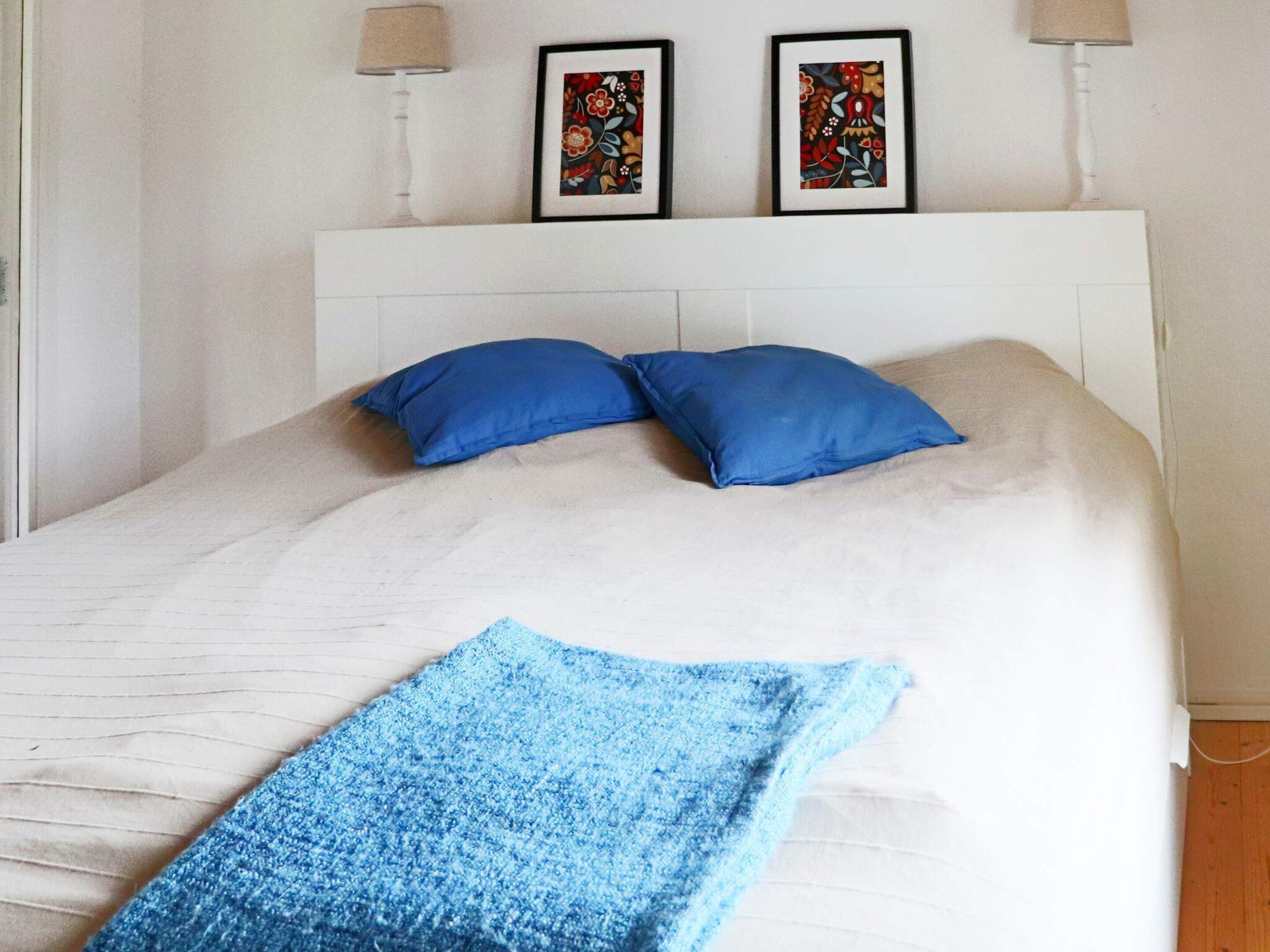 Uma cama com cabeceira branca, duas almofadas azuis e um cobertor azul.