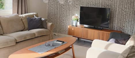 Un salón con sofá, una mesa de centro, televisor y un papel tapiz estampado.