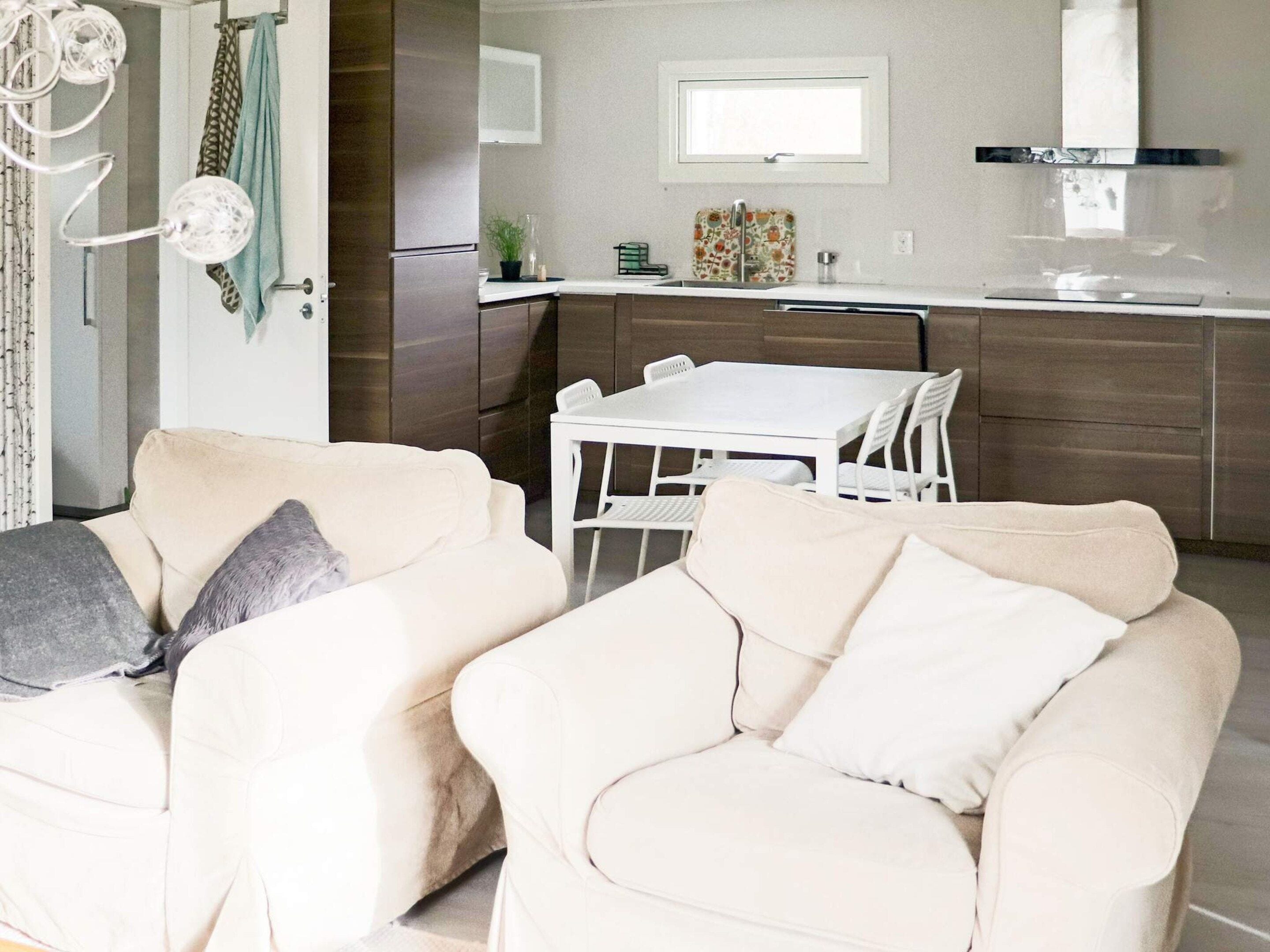 A modern kitchen with a dining area, featuring a white table and chairs, a refrigerator, and a window above the sink.