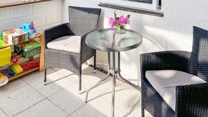 Una zona patio con sedie in vimini, un tavolo in vetro e giocattoli per bambini su uno scaffale.