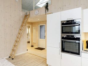 Une cuisine moderne dotée de fours encastrés et d’une échelle en bois menant à une mezzanine aménagée en espace nuit.