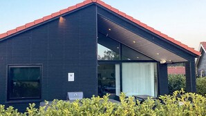 A modern building with a dark exterior, a red roof, and a covered outdoor area with seating. - 5 Star Holiday Home in Vaeggerlose (Vaeggerlose)