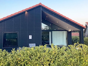 A modern building with a dark exterior, a red roof, and a covered outdoor area with seating. - 5 Star Holiday Home in Vaeggerlose (Vaeggerlose)