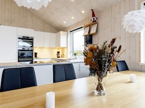 A modern kitchen with white cabinets, a central island, and a dining area with a vase of dried flowers. - 5 Star Holiday Home in Vaeggerlose (Vaeggerlose)